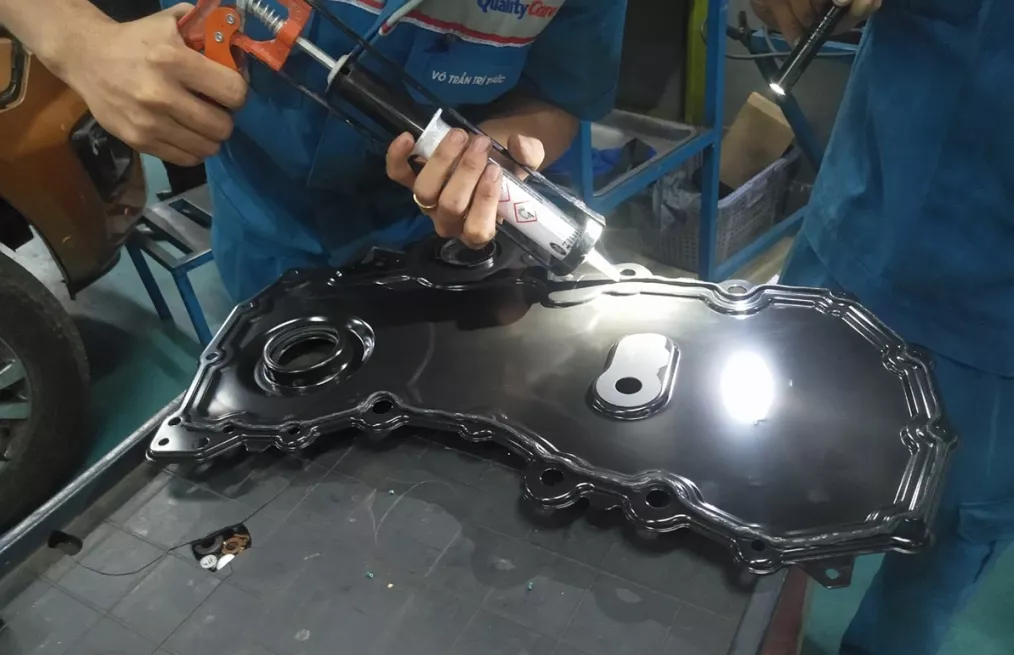 Kỹ thuật viên thực hiện bôi keo mới một động cơ xe Ford có dầu ngấm ở nắp bưởng cam.