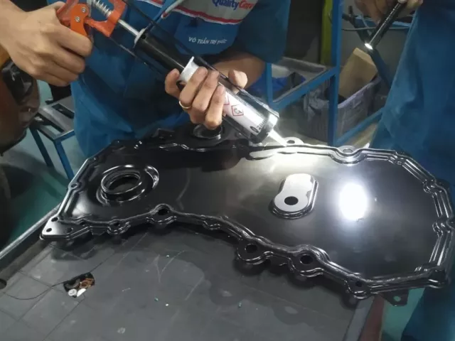 Kỹ thuật viên thực hiện bôi keo mới một động cơ xe Ford có dầu ngấm ở nắp bưởng cam.